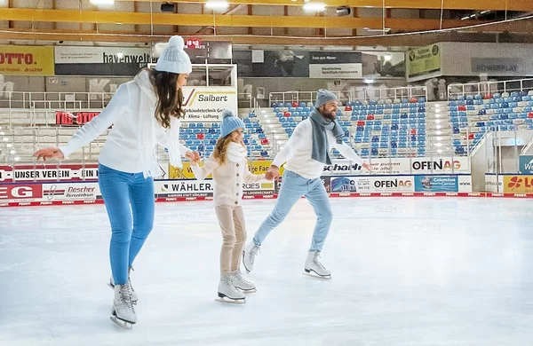 Eine dreiköpfige Familie läuft über die Eisfläche. Ihren Gesichtern ist abzulesen, dass sie Spaß haben.